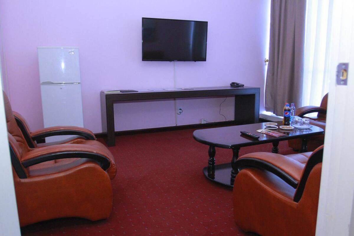 Ein Hotelzimmer mit Fernseher, kleinem Kühlschrank, Esstisch mit Stühlen und einem roten Teppich.