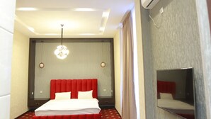 Une chambre d’hôtel avec un grand lit, un luminaire au plafond et un téléviseur fixé au mur.