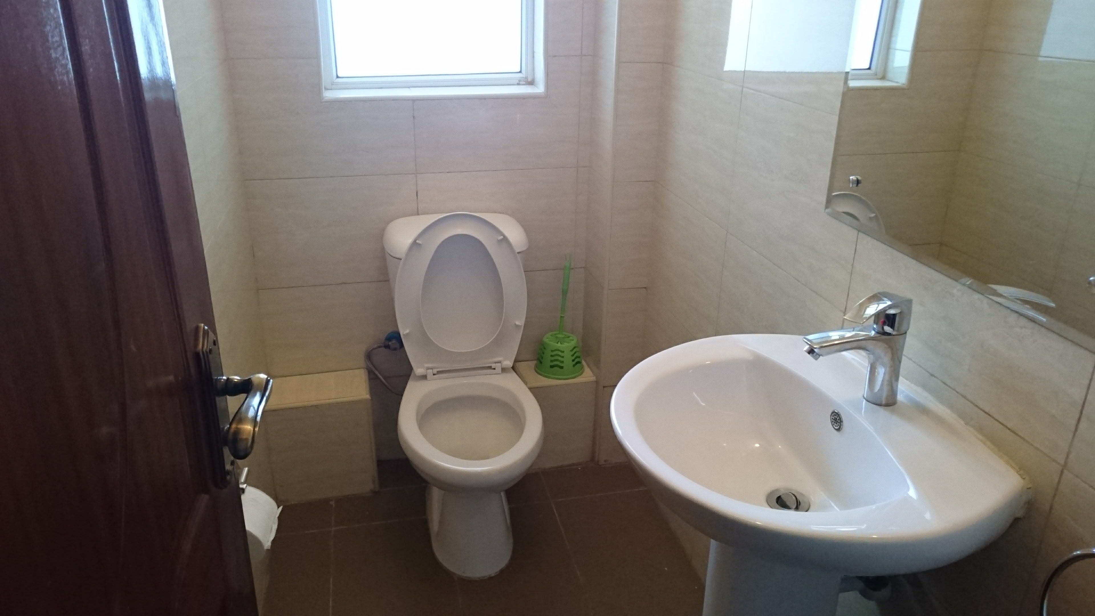 A bathroom with a toilet, sink, and a window.