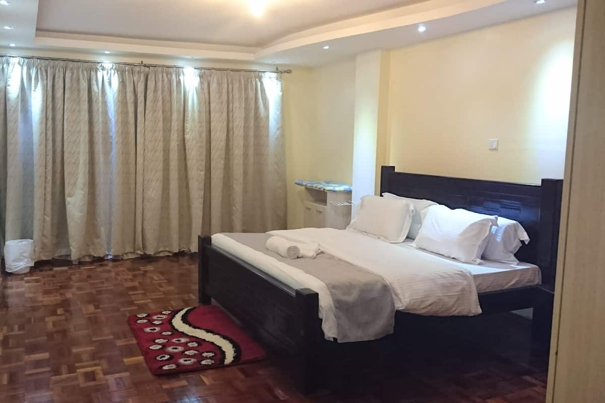 Une chambre d’hôtel avec un lit, une table de chevet, une petite table et un tapis rouge à motifs.