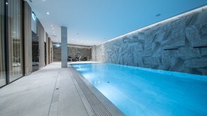 Une piscine intérieure moderne avec un mur en marbre et des portes en verre d’un côté.