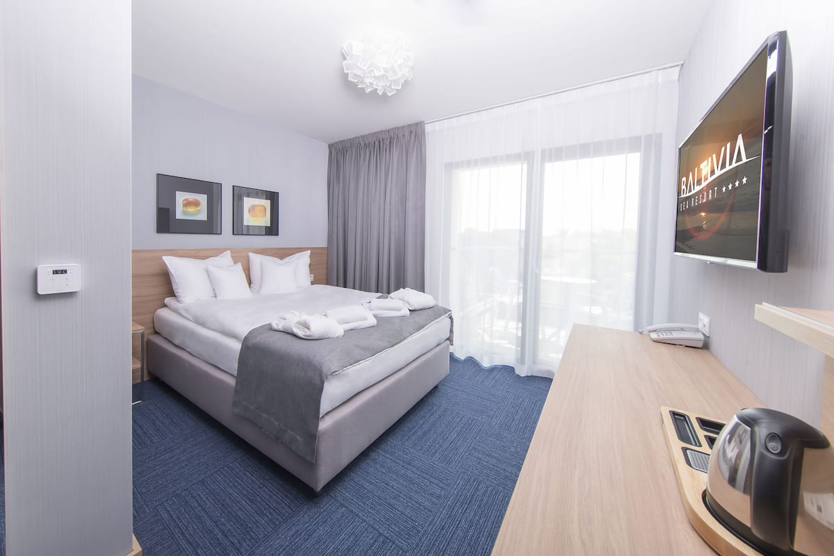 Hotellihuone, jossa on sänky, kirjoituspöytä, jossa on vedenkeitin, televisio ja ikkuna, jossa on verhot.