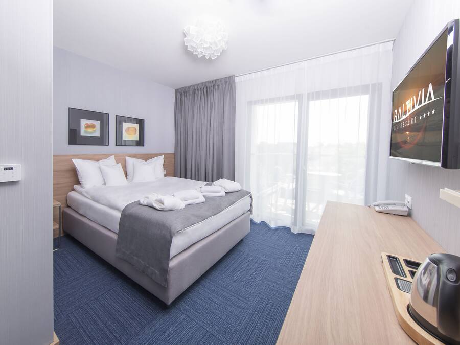Une chambre d’hôtel avec un lit, un bureau doté d’une bouilloire, une télévision et une fenêtre avec des rideaux.