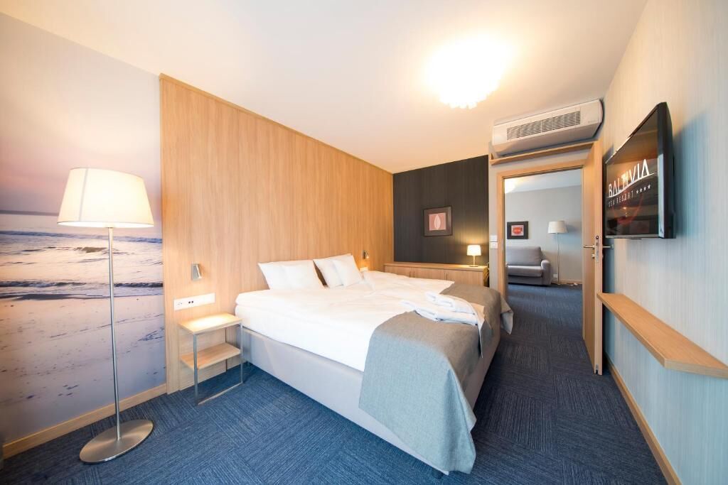 Habitación de hotel con cama, mesita de noche, lámpara, televisor y aire acondicionado instalado en la pared.