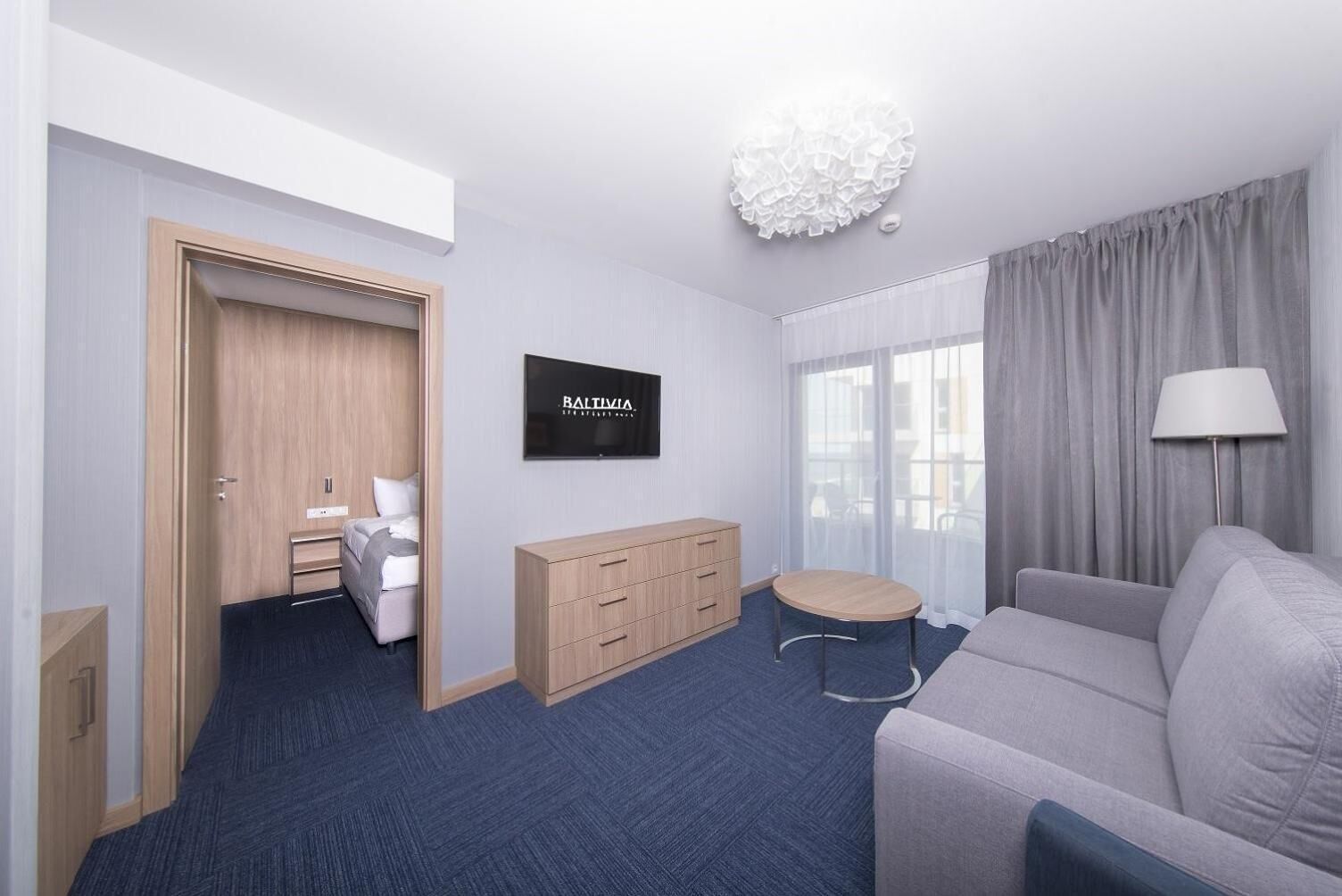 Ein Hotelzimmer mit einem Bett, einem Holzschrank, einem Fernseher, einem kleinen runden Tisch, einer Couch und einer Lampe.