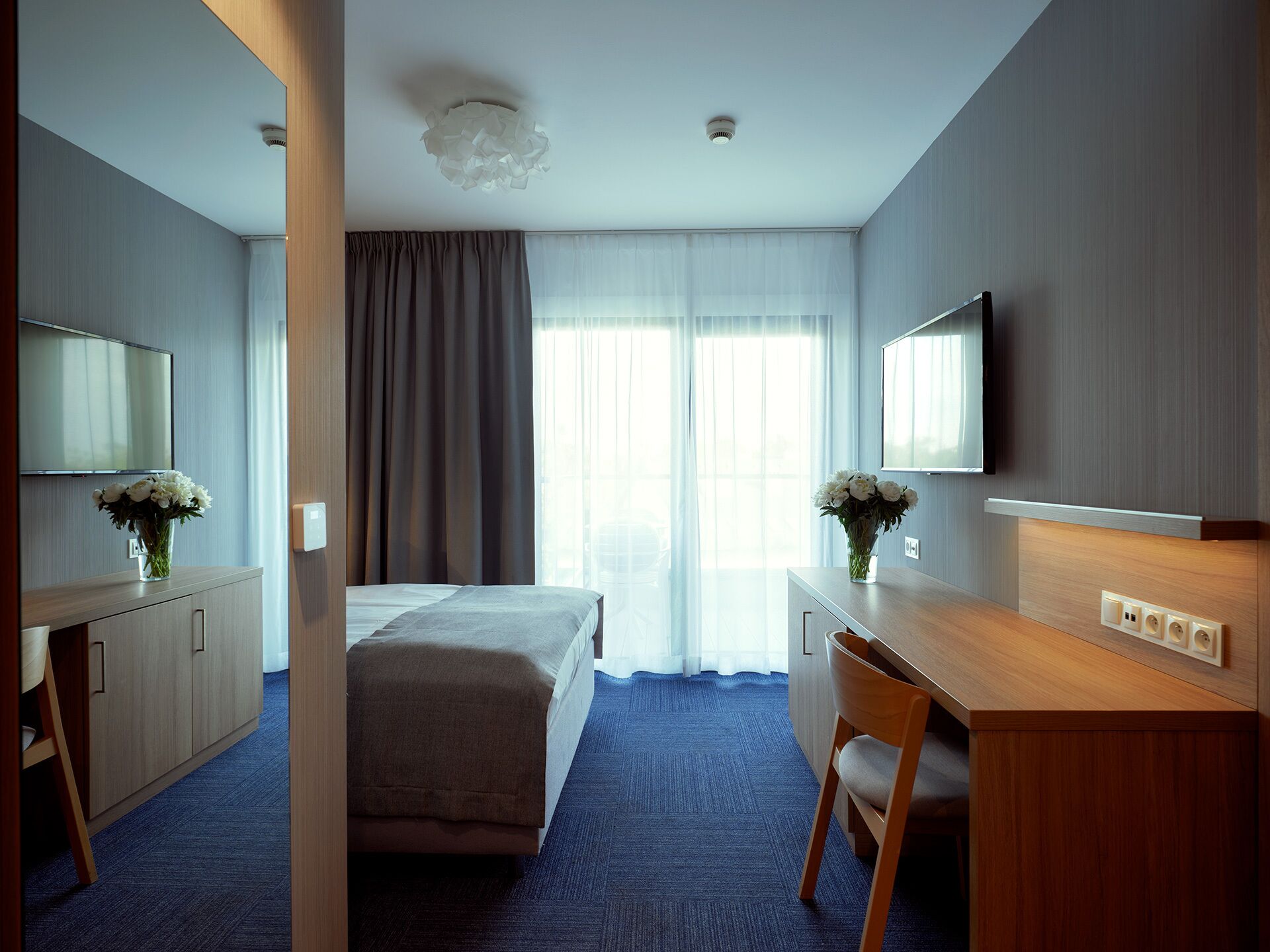 Ein Hotelzimmer mit einem Bett, einem Schreibtisch, einem Sessel, einem Fernseher und einem großen Fenster mit Vorhängen.