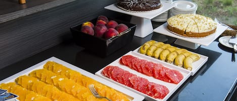 Un bufé con diversas frutas, un pastel de chocolate y una bandeja de frutas.