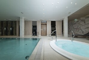 A large indoor swimming pool with a separate hot tub area, surrounded by modern architectural elements and a marble wall. - Baltivia Sea Resort (Mielno)
