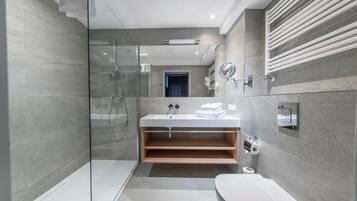 A modern bathroom with a glass-enclosed shower, a white sink with a wooden shelf, and a toilet.