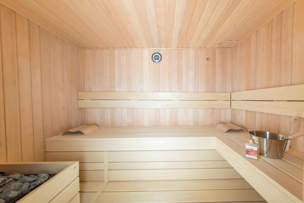 Een sauna met houten wanden en banken, een metalen emmer en een fles olie.