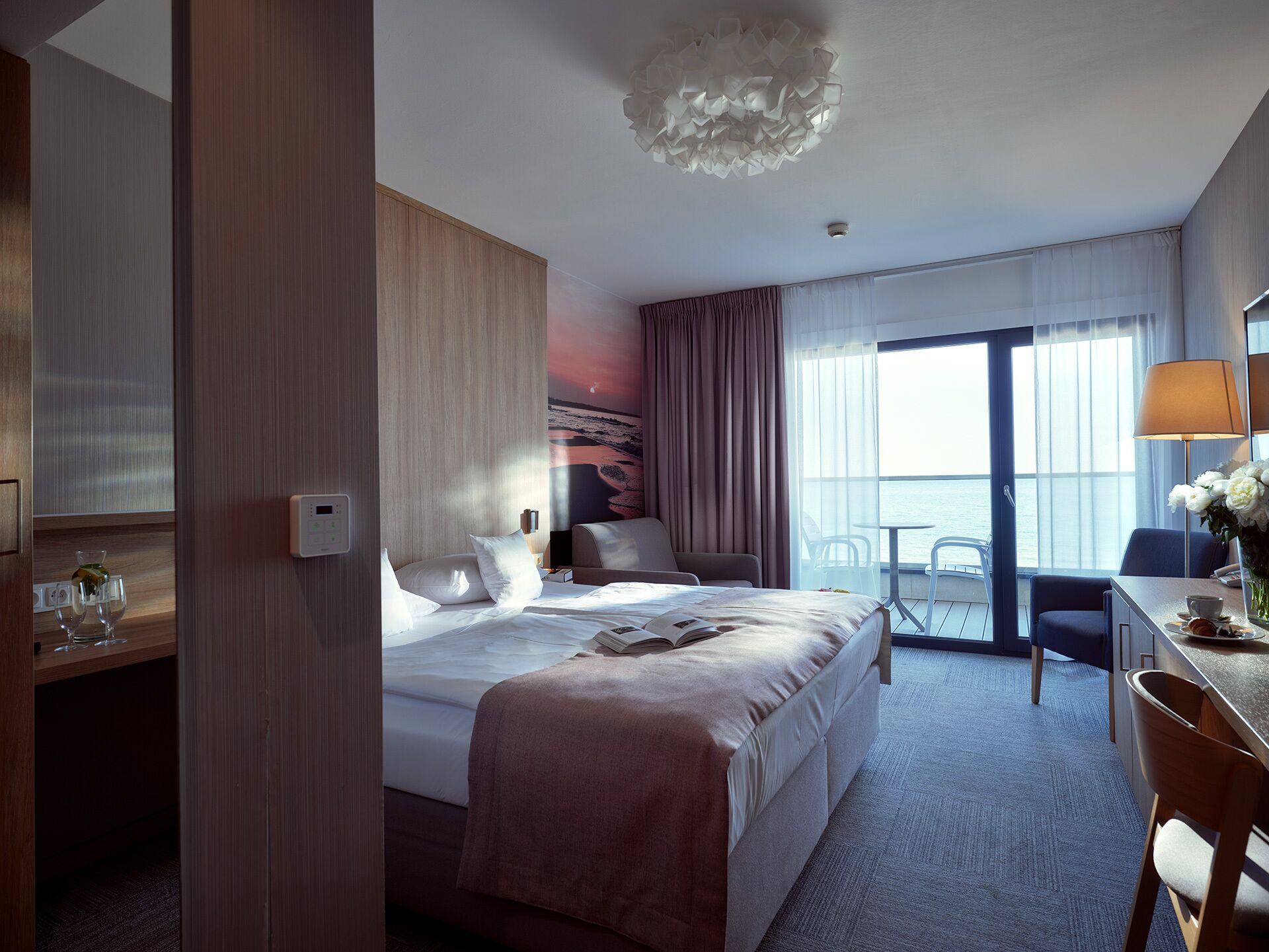 A hotel room with a bed, a desk, a chair, a table, and a view of the sea.