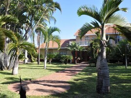 A pathway leading to a building with a red-tiled roof, surrounded by palm trees and a well-maintained lawn.