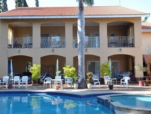 A hotel with a swimming pool, outdoor seating, and a two-story building with balconies.
