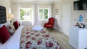 Une chambre à coucher avec un lit, un fauteuil rouge, un ventilateur de plafond, une télévision et une petite armoire blanche.