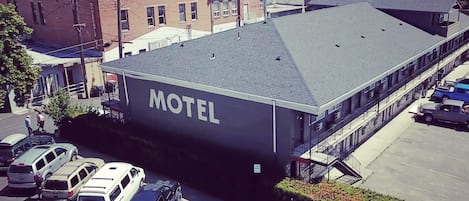 Um motel com teto plano, estacionamento com vários carros e vista da área circundante, incluindo outros edifícios e vegetação.