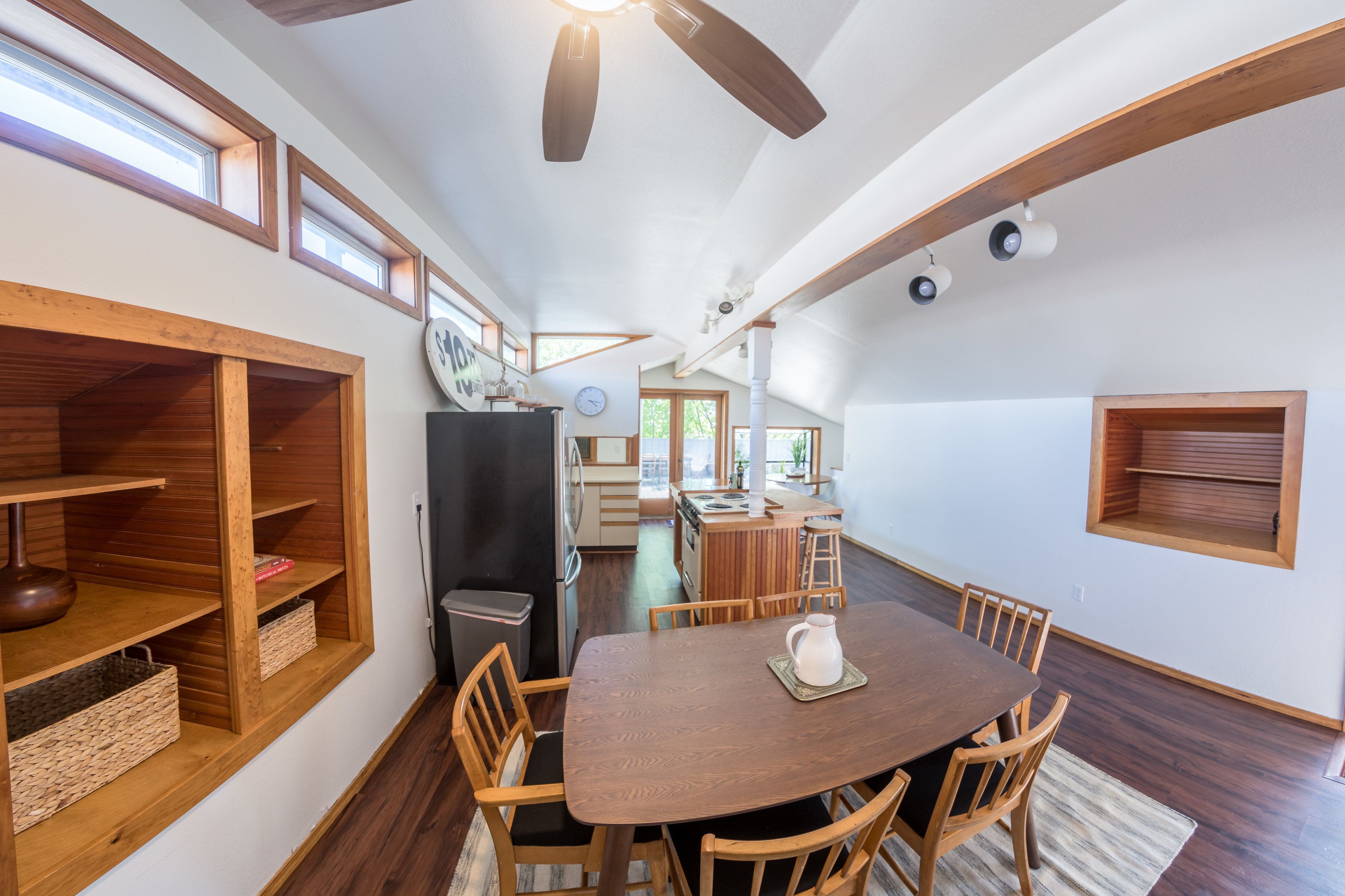 A spacious dining area with a wooden table and chairs, a kitchen in the background, and built-in wooden shelves.