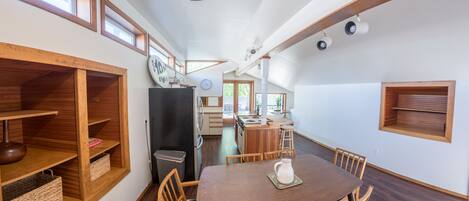 A spacious dining area with a wooden table and chairs, a kitchen in the background, and built-in wooden shelves.