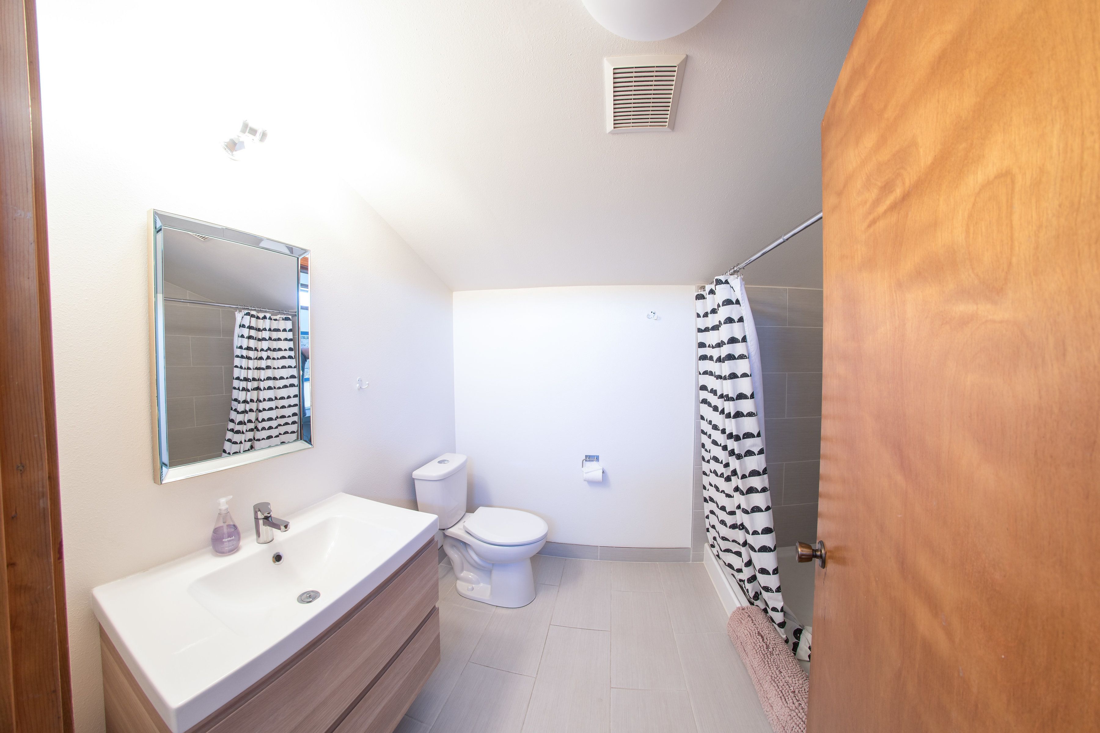 A bathroom with a sink, mirror, toilet, and shower curtain.