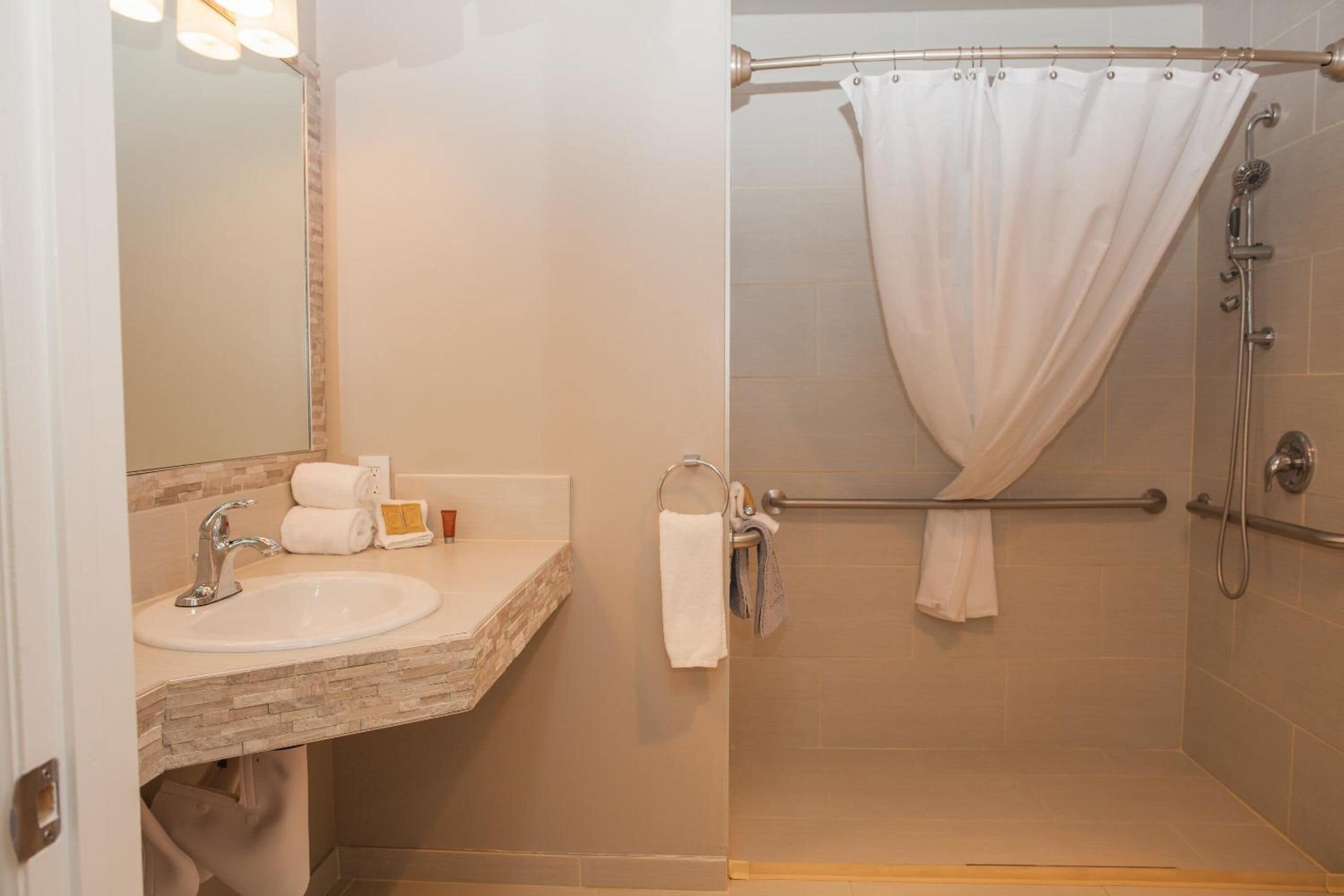 A bathroom with a sink, mirror, and shower area.
