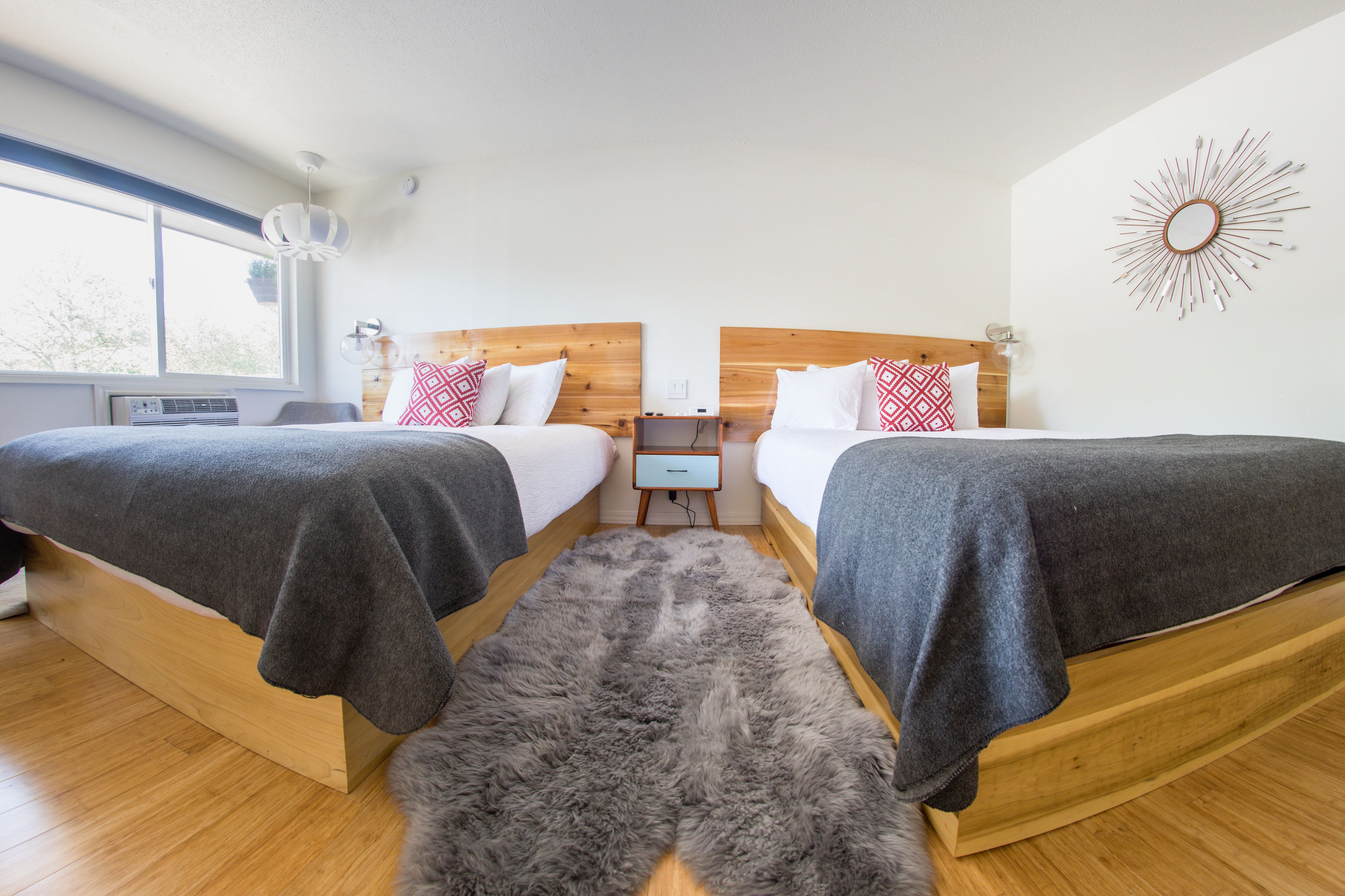 Een moderne slaapkamer met twee bedden, een houten hoofdbord, een klein nachtkastje en een groot raam.