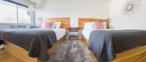 Un dormitorio moderno con dos camas, un cabecero de madera, una mesita de noche pequeña y un ventanal amplio.