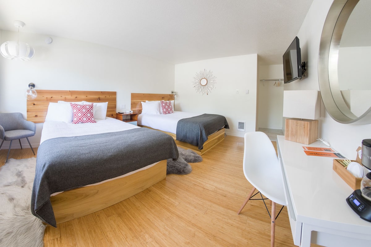 A hotel room with two beds, a desk, a chair, a TV, and a mirror.