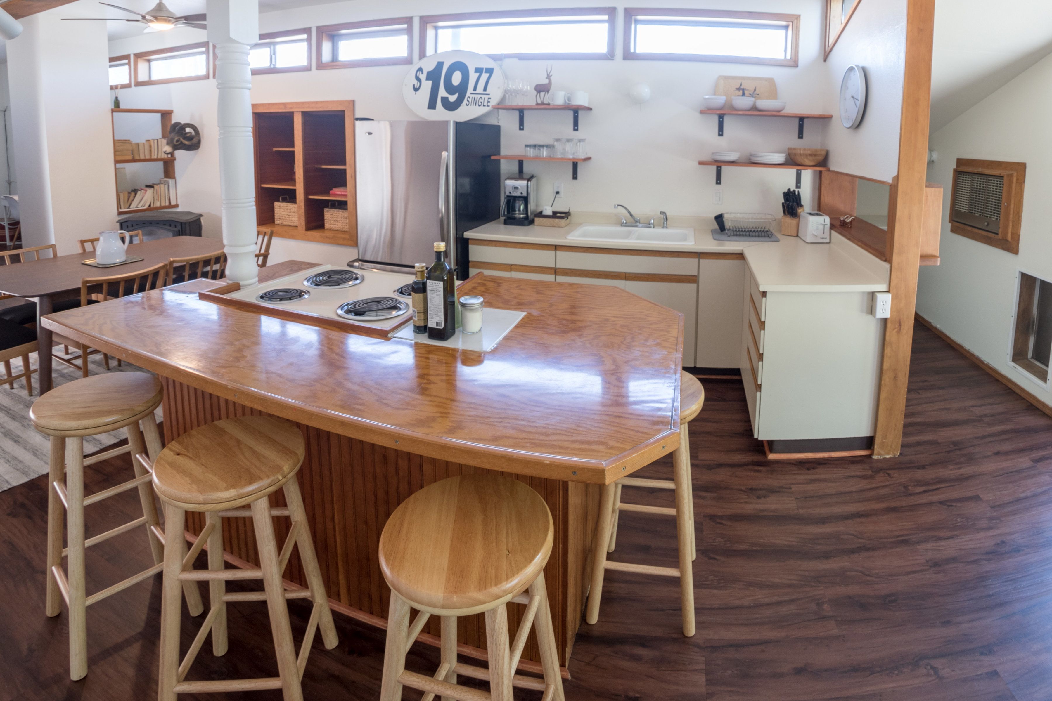 A spacious kitchen with a central island, wooden stools, a refrigerator, and a coffee maker.