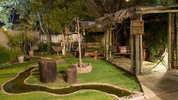 A garden with a pond, wooden structures, and a covered seating area. - La Boheme Guesthouse (Bloemfontein)