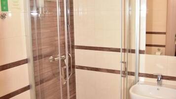 A corner shower with a glass door, a sink, and a mirror.