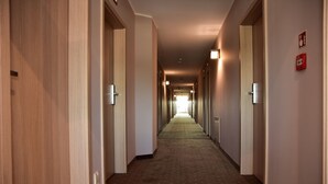 A hotel hallway with wooden doors, carpeted floors, and emergency exit signs. - Hotel Nekla (Nekla)