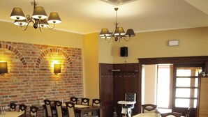 A dining area with brick walls, multiple tables, chairs, and chandeliers. - Hotel Nekla (Nekla)