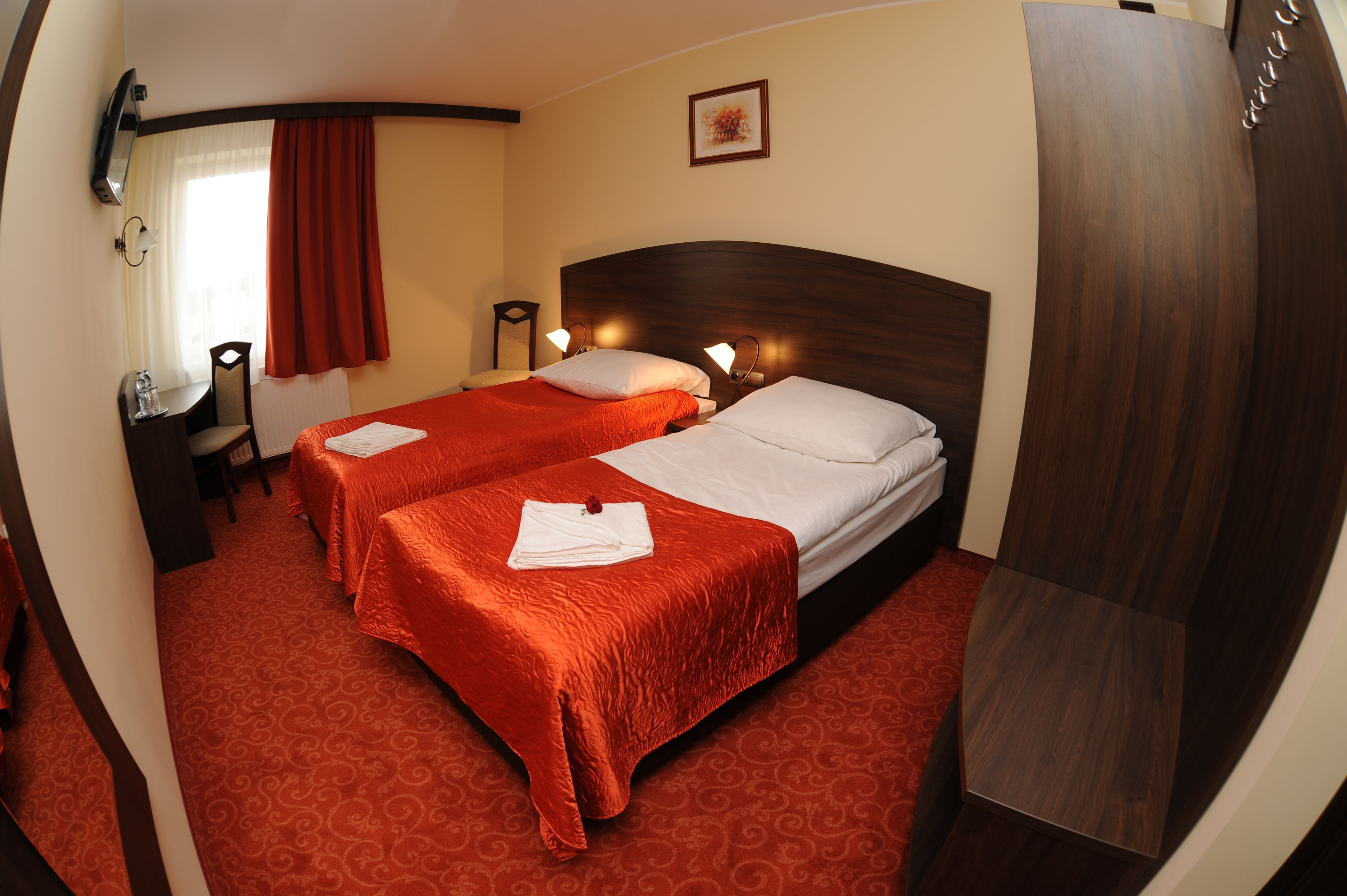 Une chambre d’hôtel avec deux lits, un bureau, une chaise, une télévision et une fenêtre avec des rideaux.