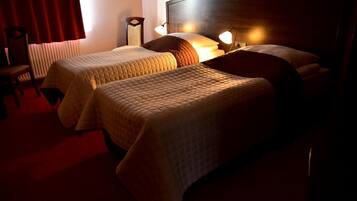 Quarto de hotel com duas camas, cabeceira de madeira, cortina vermelha e abajur.