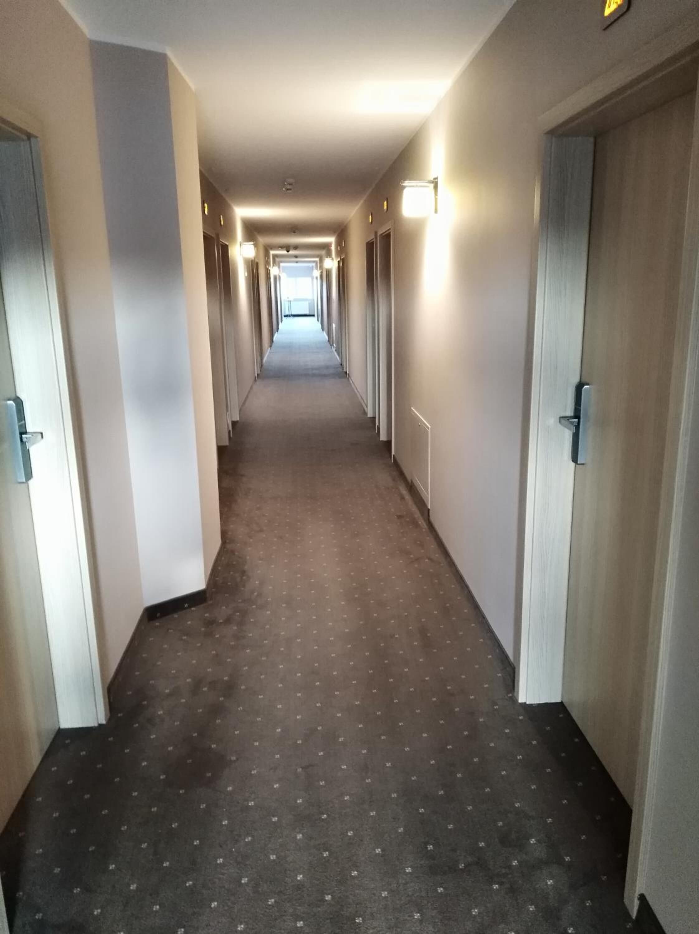 A long, narrow hotel corridor with carpeted floors and doors on both sides.