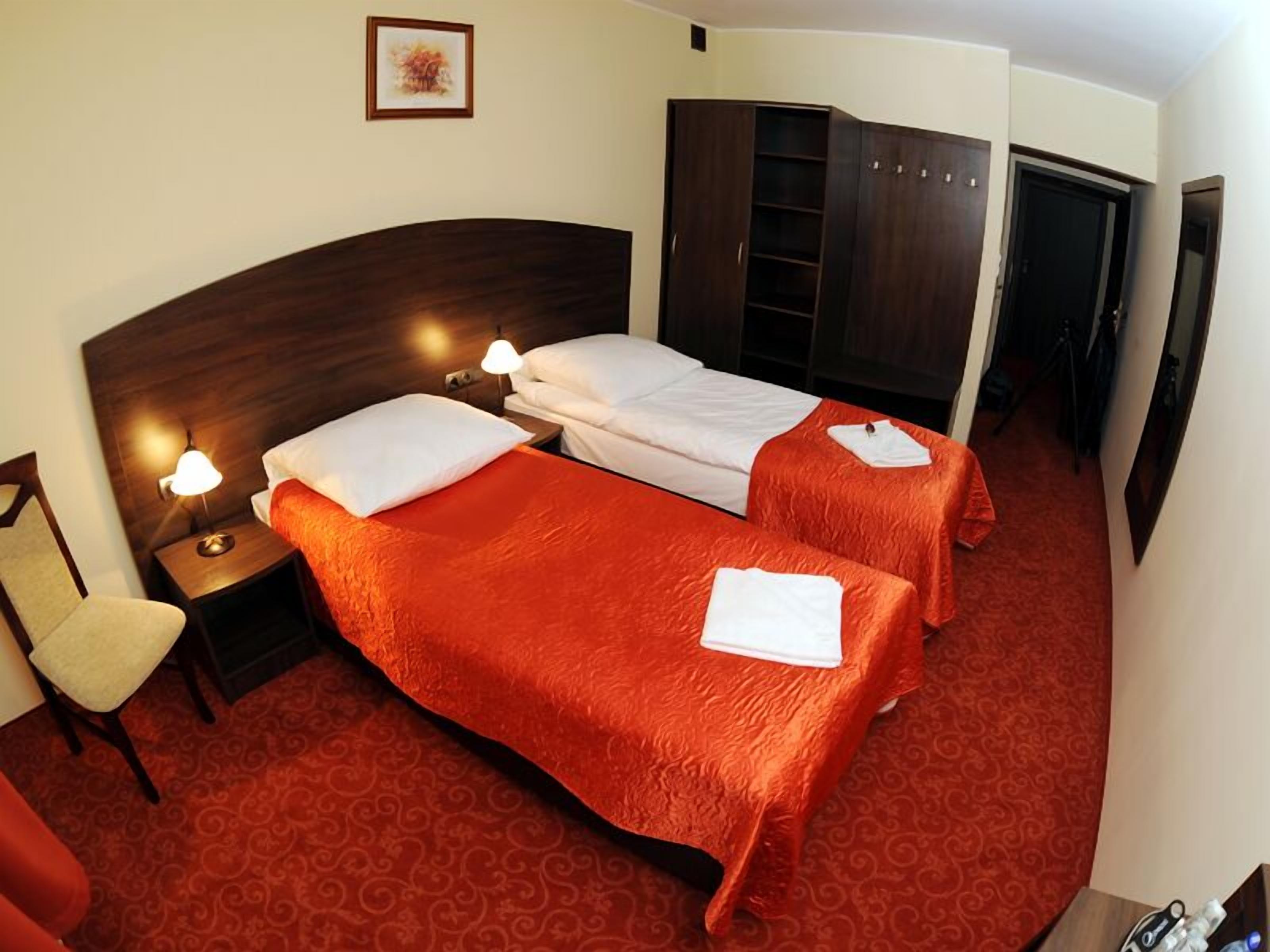 A hotel room with two beds, a wooden headboard, a red carpet, and a wardrobe.