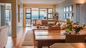 Amplia sala de estar con una mesa de comedor de madera, un conjunto de sofás y vistas al océano a través de amplias puertas correderas.
