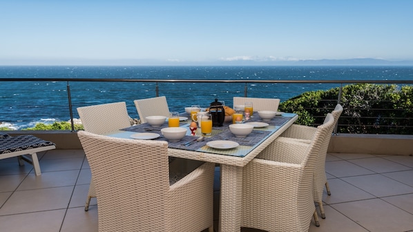 Mesa de desayuno con alimentos en un balcón con vista al mar.