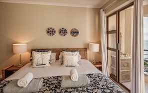 Habitación de hotel con una cama grande, dos lámparas fijadas a la pared, vista al mar a través de un ventanal amplio y decoración en las paredes.