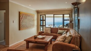 Una sala de estar con una mesa de centro de madera, un sofá marrón y un ventanal con vistas al mar.