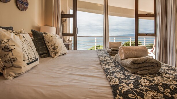 Habitación de hotel con una cama grande, vistas al océano y un balcón con cortinas.