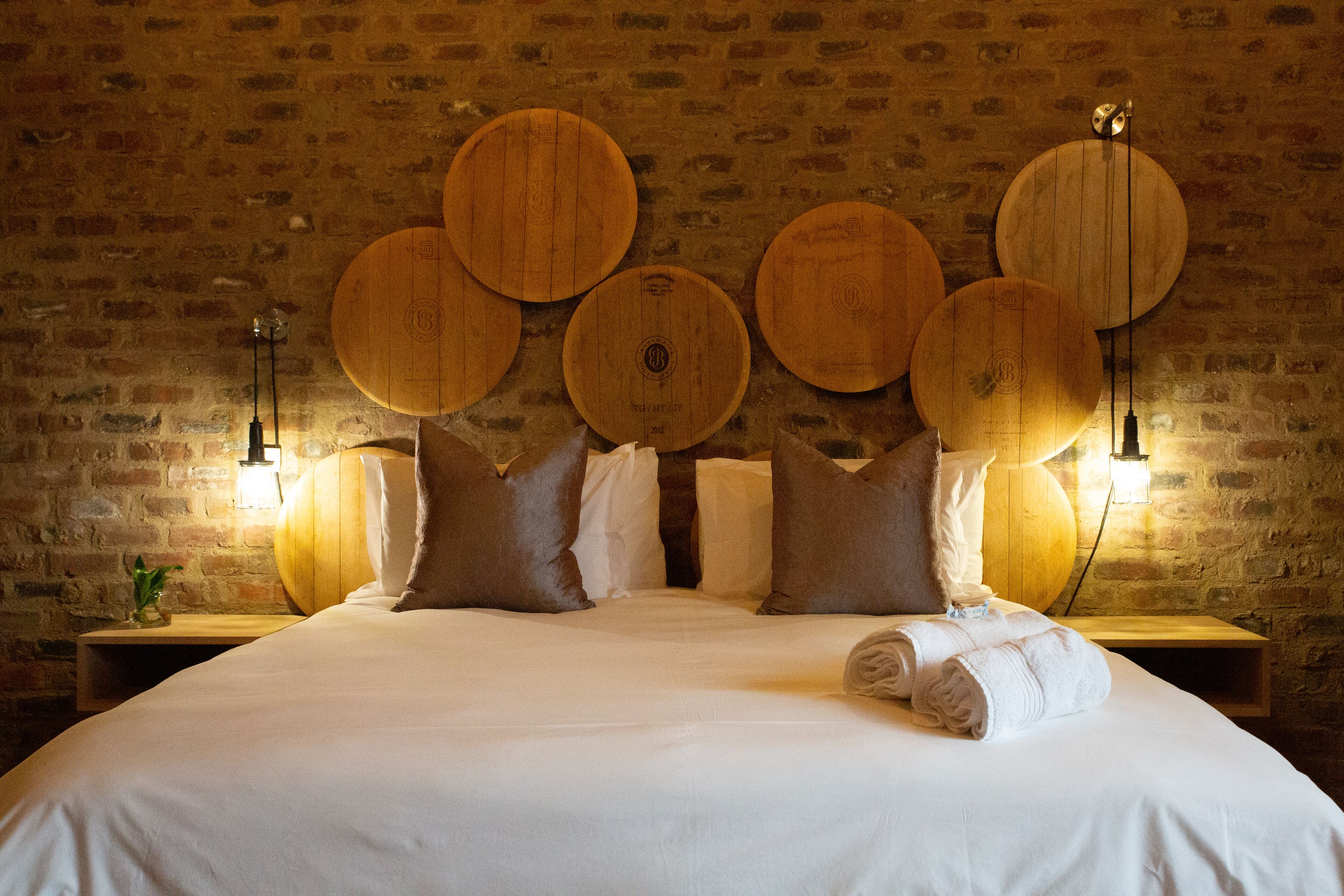 A hotel room with a brick wall, a large bed with white linens, multiple pillows, and wooden wall decor.