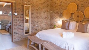 A bedroom with a brick wall, a wooden headboard, a large bed, a bedside table, and a bench. - Execustay (Mbombela)