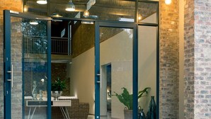 A modern building entrance with glass doors, a visible seating area with a table and chairs, and a potted plant. - Execustay (Mbombela)