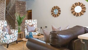 A living room with two patterned armchairs, a leather sofa, and a small round table with decorative items. - Execustay (Mbombela)