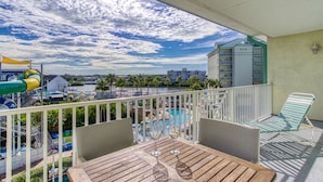 A balcony with a view of a pool area, a table with two glasses, and a chair.