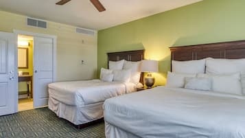 Quarto de hotel com duas camas, um ventilador de teto, mesa de cabeceira com abajur e banheiro visível por uma porta aberta.