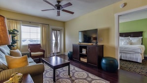 A hotel room with a sofa, armchair, coffee table, television, and a bed.