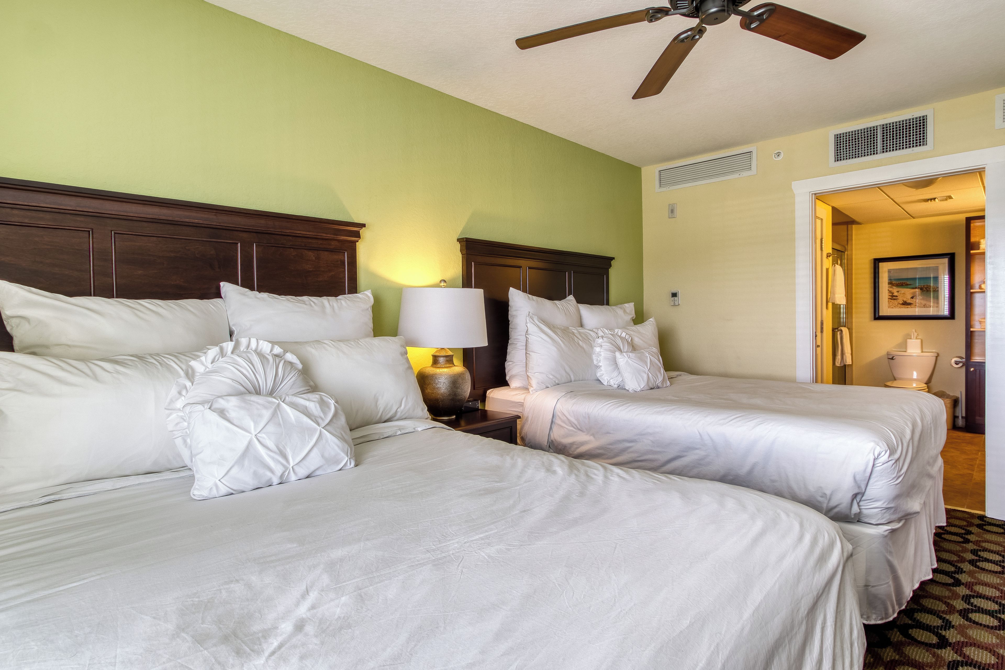 Une chambre d’hôtel avec deux lits, un ventilateur de plafond et une table de chevet avec une lampe.