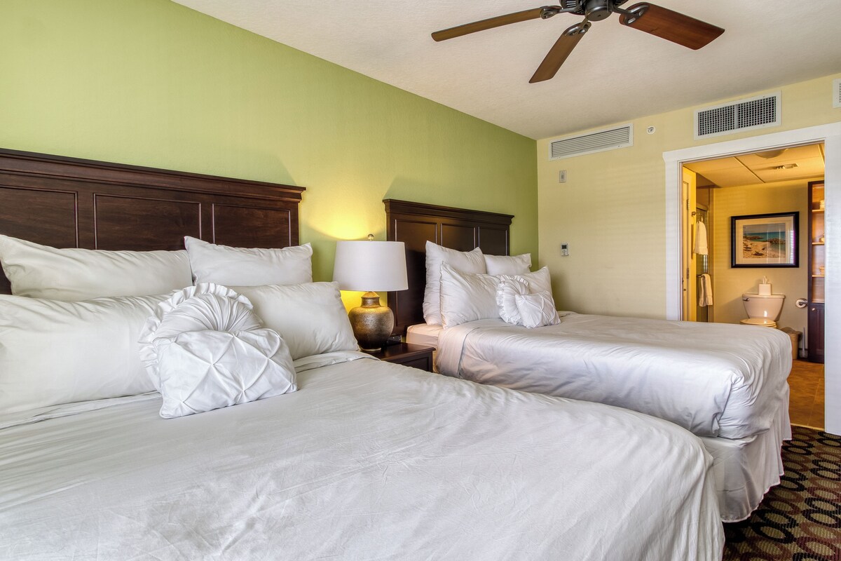 Una habitación de hotel con dos camas, un ventilador de techo y una mesita de noche con lámpara.