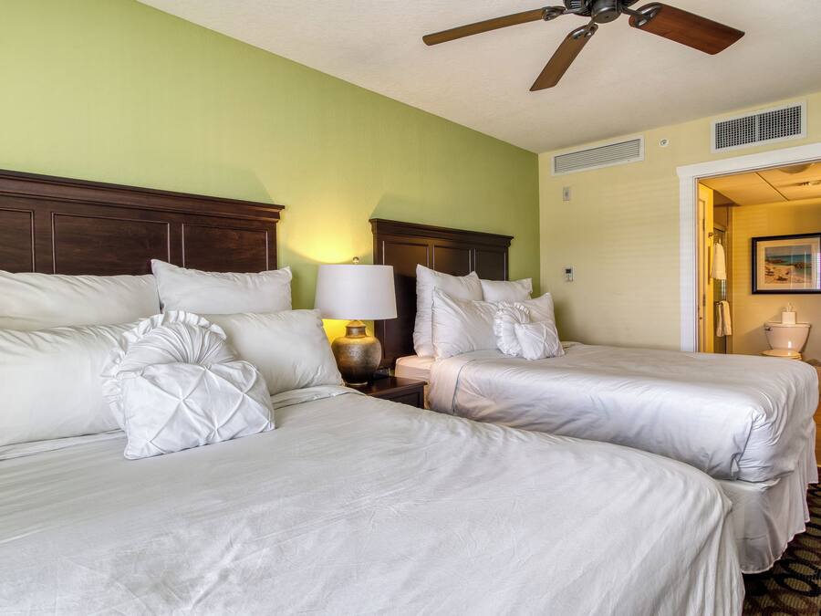 A hotel room with two beds, a ceiling fan, and a nightstand with a lamp.